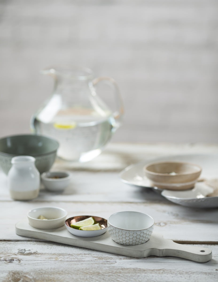 An image of a jug of water, modern bowls and rustic condiments on a faded white table