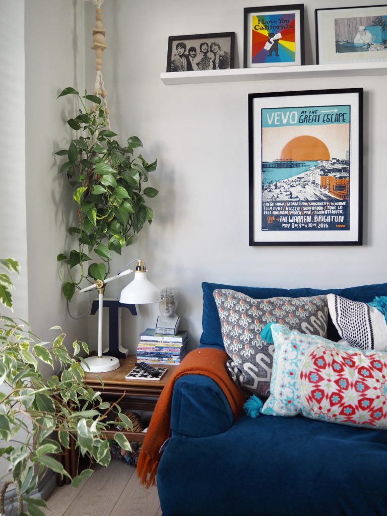 Blue velvet sofa with orange throw and gallery wall