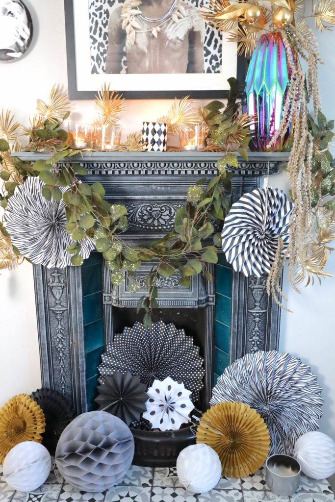 Fireplace & mantelpiece dressed with garland and paper decorations with cocktail gold trolley. black and white art. 7 cool Zoom Party Styling Ideas