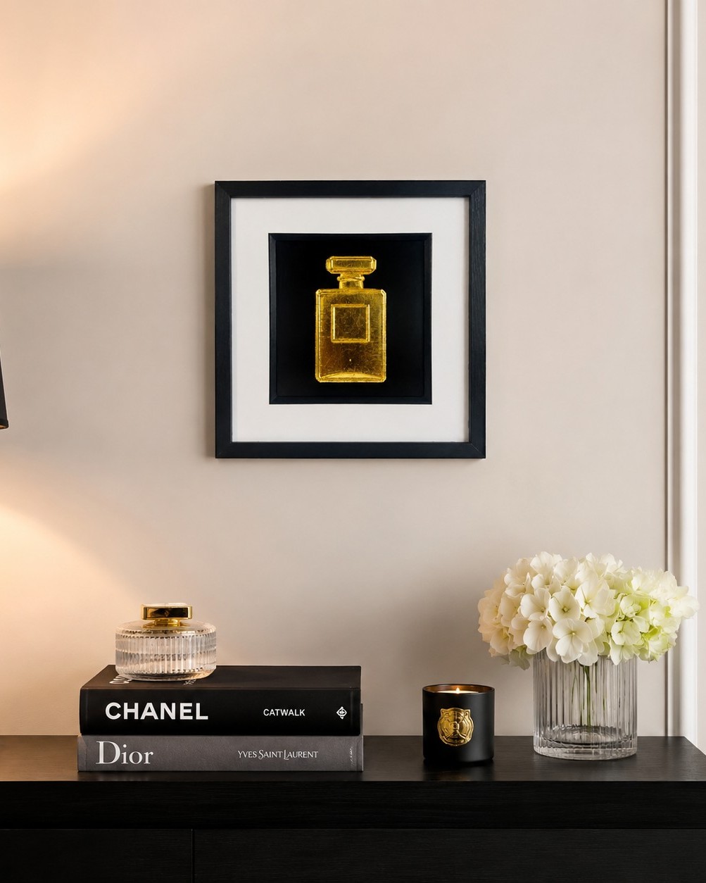 How to choose wall art for your home:. Gold perfume bottle wall art in a black frame styled with fashion books and flowers